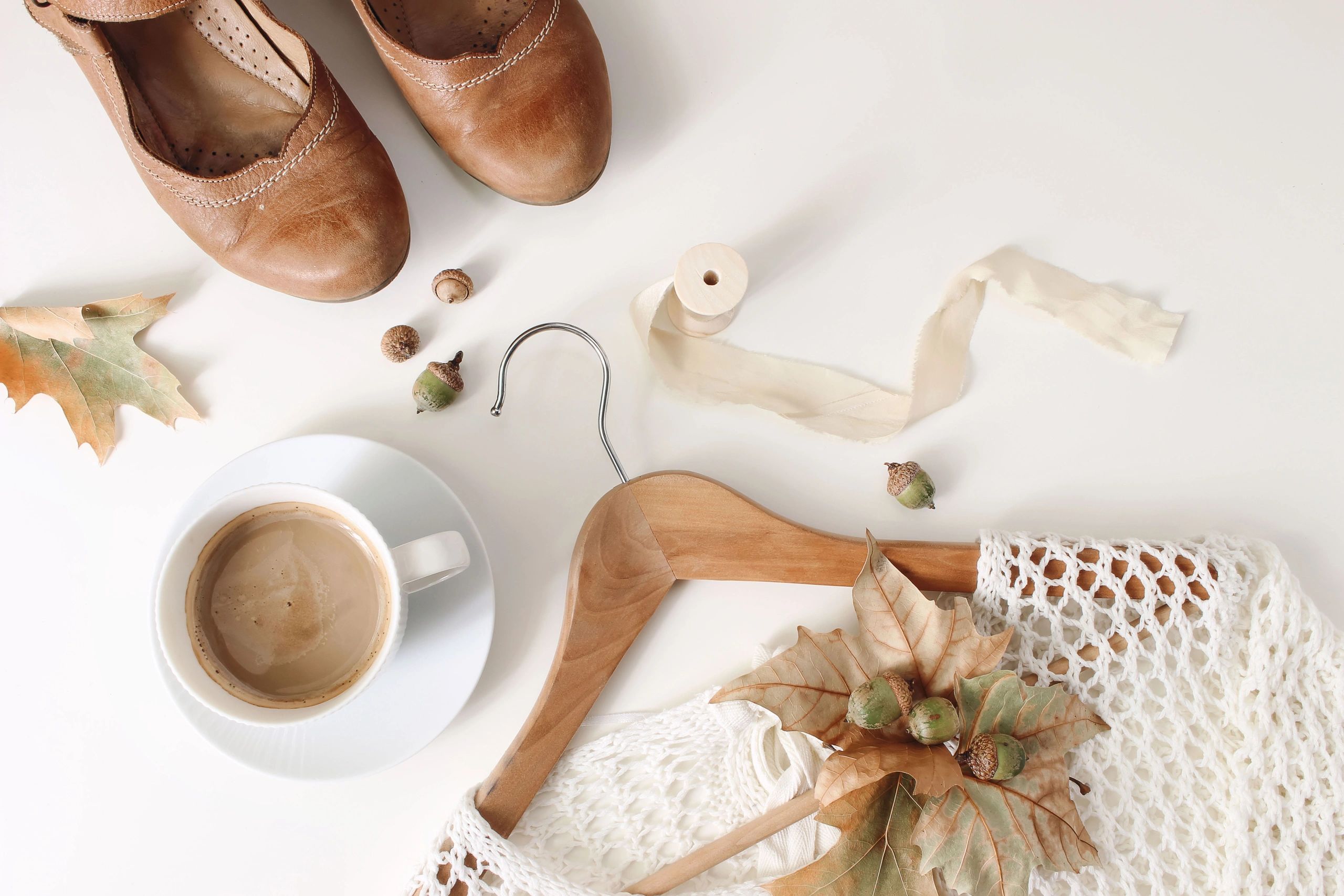 Neutral fashion flat lay with sweater, shoes, and coffee on a white background